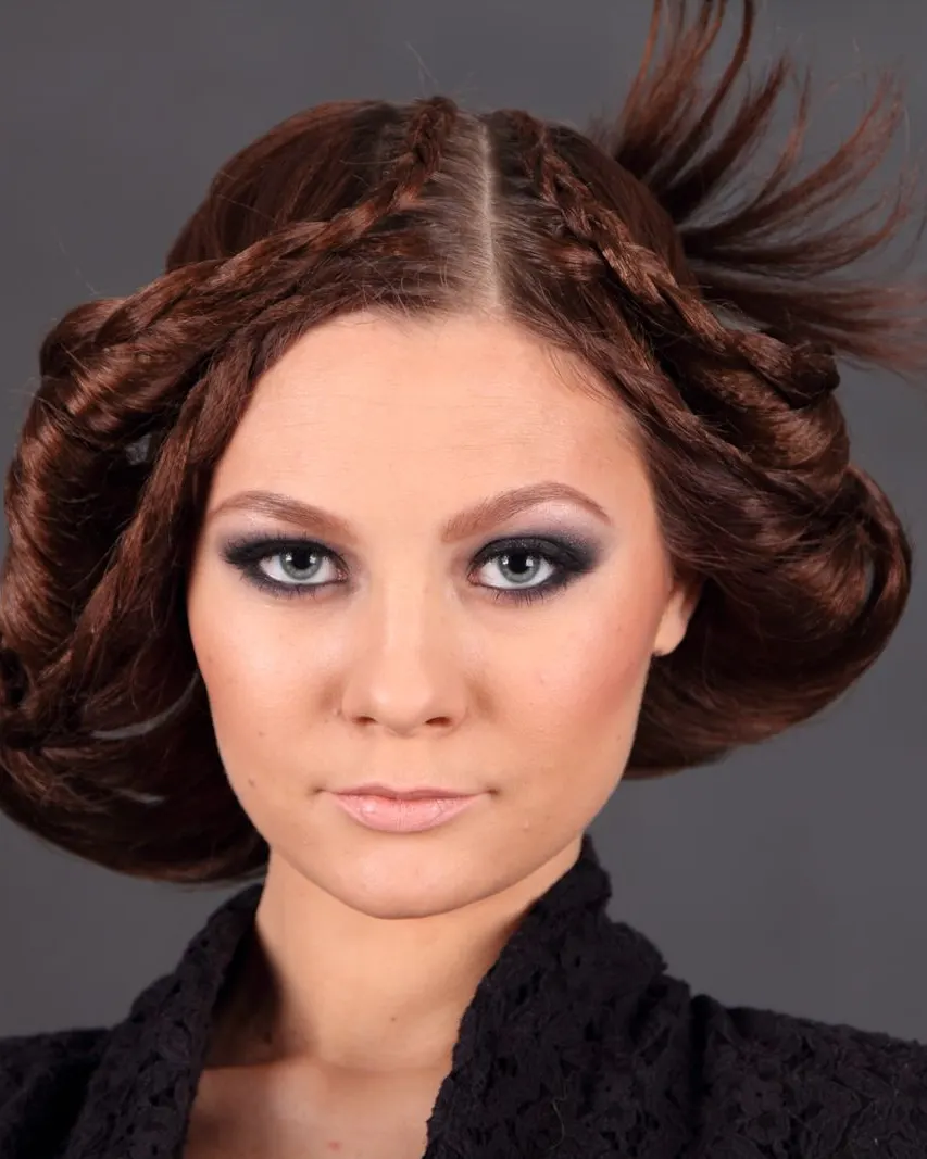 A studio portrait of a woman with an intricately braided, sculptural hairstyle and soft smoky eye makeup